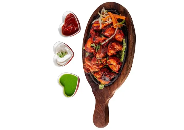 Spicy chicken tikka on a wooden paddle with chutneys